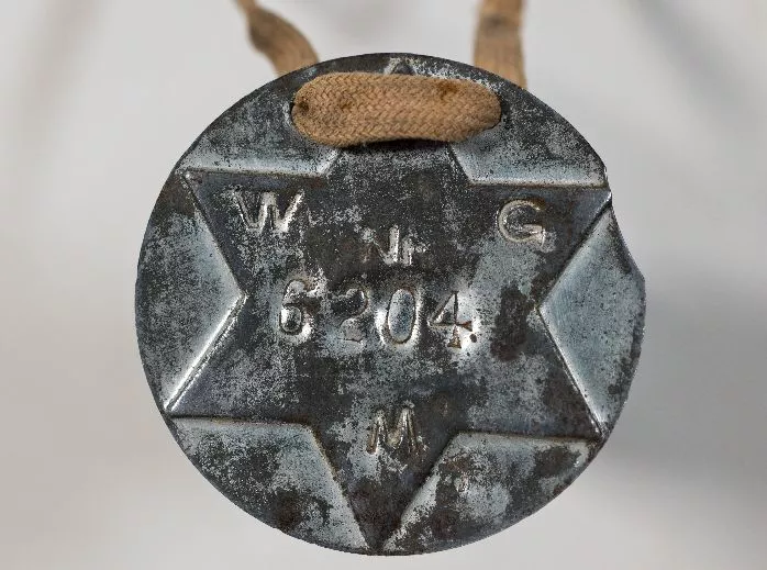 Metalinis žetonas, privalomas nešioti Vilniaus geto kaliniams nuo 1943 m. vasario 7 d. Nuotrauka iš Valstybinio Vilniaus Gaono žydų muziejaus